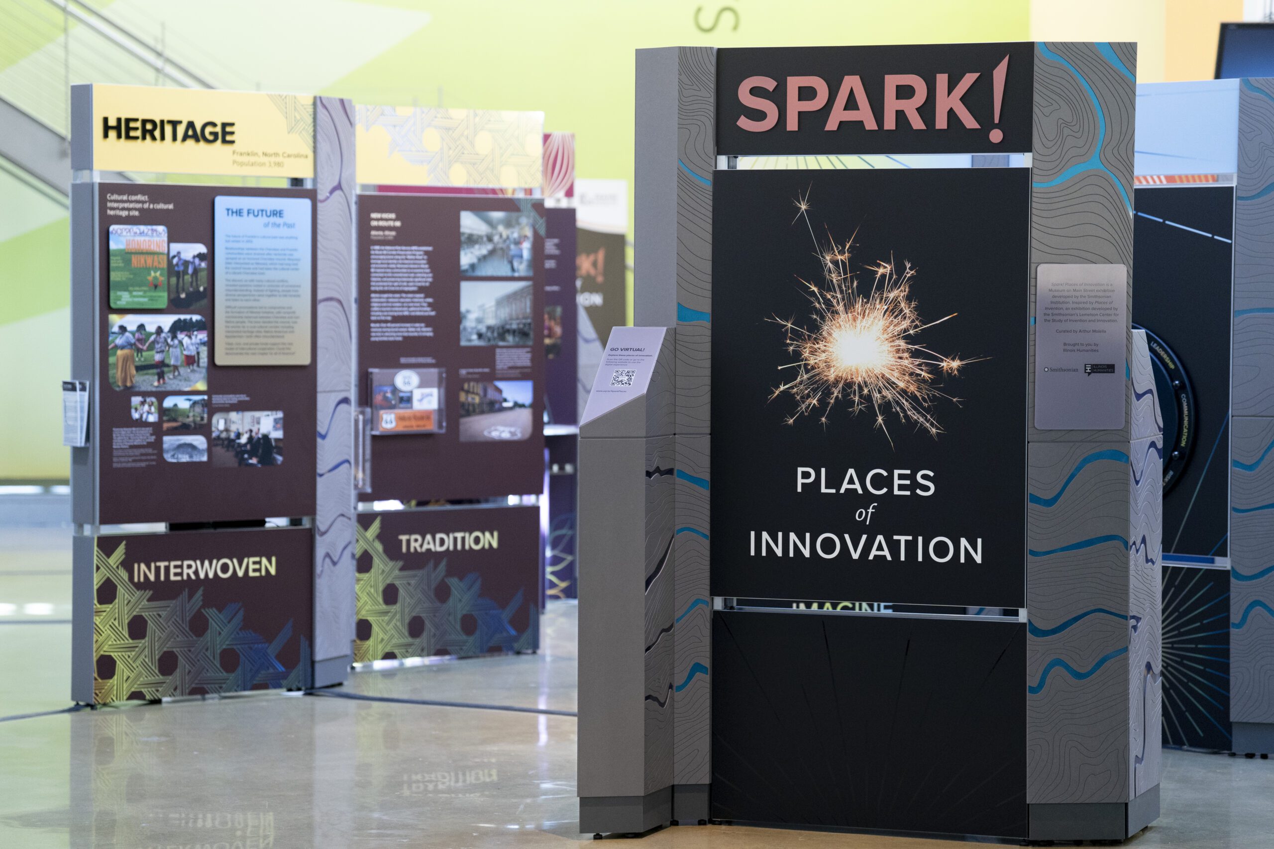 Photograph of SPARK! Smithsonian exhibit, which features pictures, unreadable text, and key words like INTERWOVEN and TRADITION