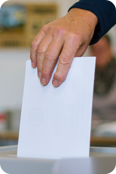close up image of a hand putting a ballot into a ballot box